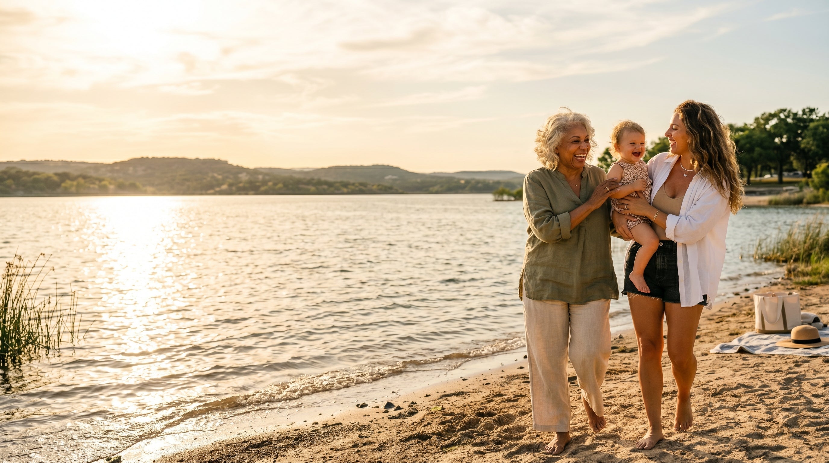 2 women, a grandmother and a mom with  a baby stand on the beach in the late afternoon feeling happy.