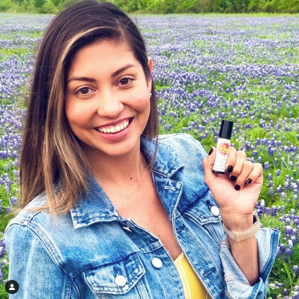 a young woman holding a small bottle of rich oil in a field of bluebonnets
