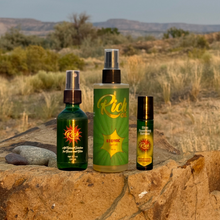 Load image into Gallery viewer, Three green bottles with labels on a rock in a desert landscape
