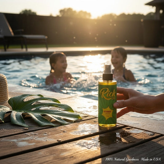 The Rich Oil Atomic Oil natural sun maximizer tanning oil bottle held by a hand by a pool with children playing.
