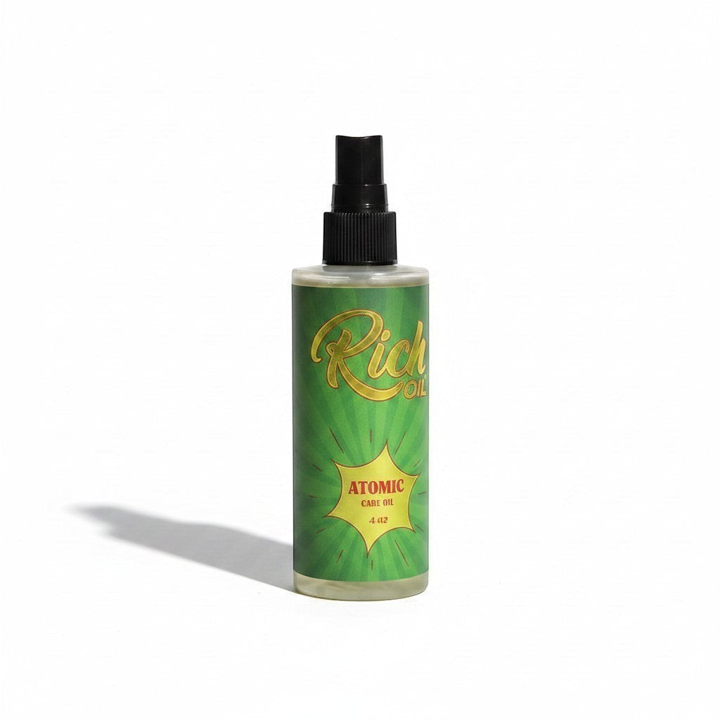 The Rich Oil Atomic tanning oil in a clear bottle with a green label featuring sunburst rays and gold text. Supports Vitamin D conversion and skin hydration.