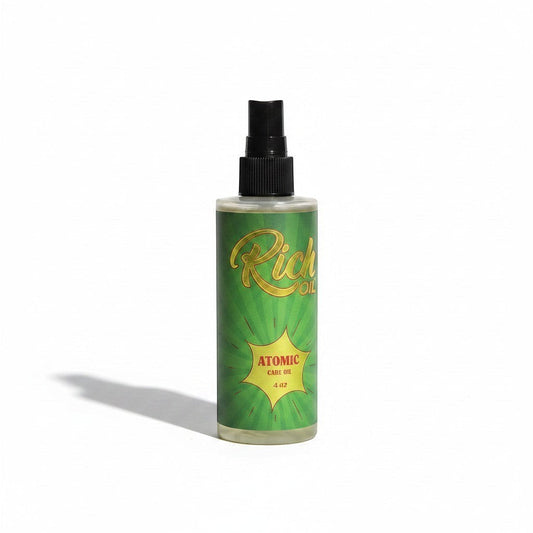 The Rich Oil Atomic tanning oil in a clear bottle with a green label featuring sunburst rays and gold text. Supports Vitamin D conversion and skin hydration.